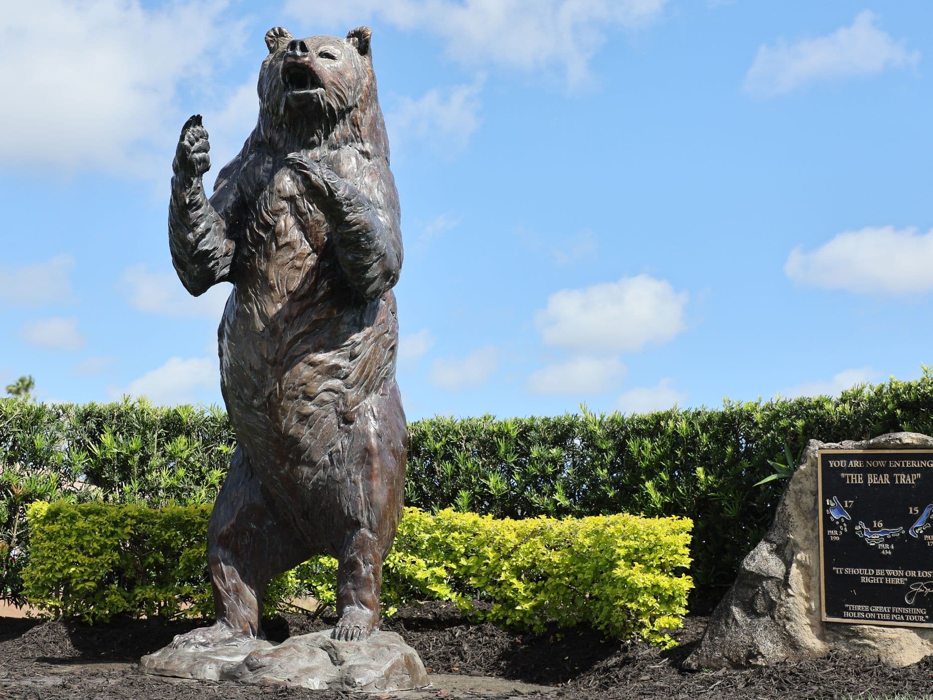 Bronze bear statue standing on hind legs beside The Bear Trap golf course sign.